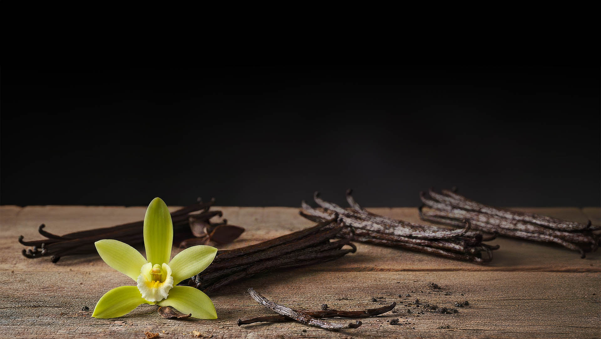 Vainas de vainilla y flor de vainilla en mesa rústica